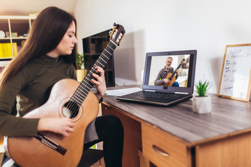 focused girl playing acoustic guitar and watching online course on laptop while practicing at home. 