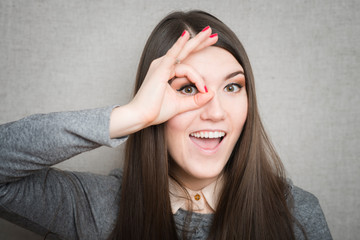 Wall Mural - Young happy woman holding her hand over her eye as glasses and  looking through fingers