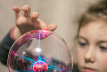 The child touches the plasma ball with his finger. Selective focus.