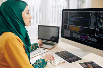 Wall Mural - young muslim coder using computer and laptop when testing new program whe wrote