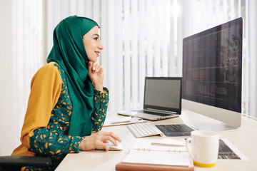 Wall Mural - smiling muslim young woman in traditional dress enjoying working on new project for it company