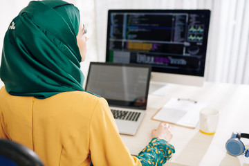 Wall Mural - young female muslim code in beautiful emerald hijab working on computer at her office desk