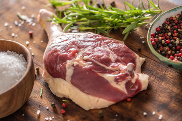 Wall Mural - Close-up view of a raw unskinned duck leg with pepper, rosemary and salt on a dark wooden background