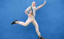 Senior Crazy Man Jumping While Listening Music With Wireless Headphones - Hipster Old Guy Having Fun Dancing Outdoor - People Happiness And Elderly Technology Addicted Concept - Blue Background