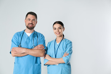 Poster - Mature doctor and young nurse against light background