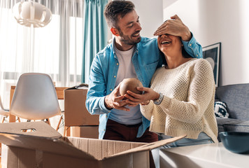 Wall Mural - Smiling young couple move into a new home sitting on floor and unpacking boxes of their belongings.