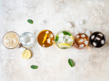 Flat Lay Of Various Refreshing Drinks In Glasses With Ice. Apple Juice, Cola, Homemade Lemonade, Iced Coffee, Iced Tea And Sparkling Water On A Beige Background. Top View