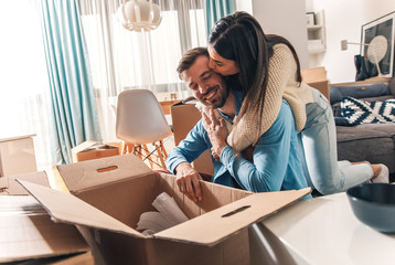 Wall Mural - Smiling young couple move into a new home sitting on floor and unpacking boxes of their belongings.