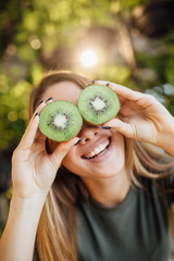 Happy young caucasian woman holding kiwi in front of eyes