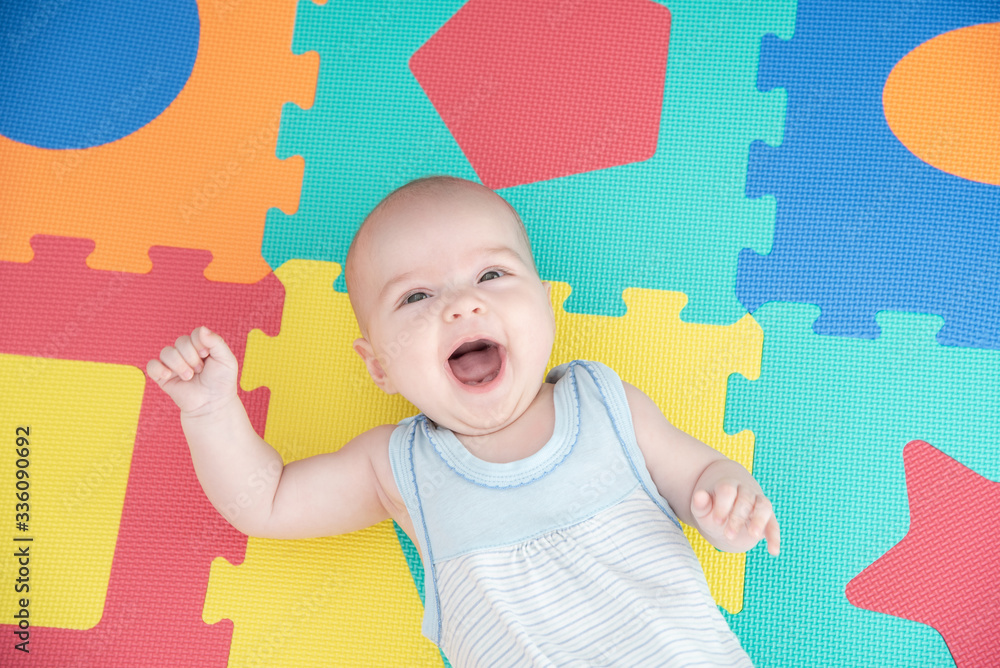 Laughing child on a colored rubber mat puzzle for playing foam with geometric figures - obrazy, fototapety, plakaty 