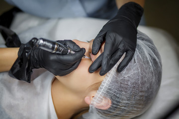 Wall Mural - Permanent make up eyeliner procedure, applying on young girl. Close-up. Young beautiful woman making permanent makeup in cosmetology salon. Young girl applying permanent eyeliner in beauty studio