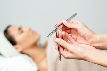 Wall Mural - Tweezers in hands of beautician on background of woman before eyelash extensions procedure.