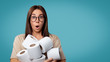 © South House Studio - Brunette woman in glasses holds a lots of toilet paper, she opened her mouth in a surprise, copy space, isolated over blue background