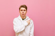 © bodnarphoto - Surprised young man in white casual clothes looks into the camera and points his finger away at copy space isolated on pink. Guy in the white hoodie is pointing his finger at an empty seat.