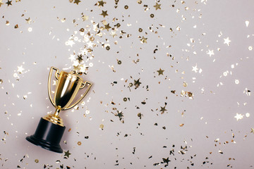 sparkles grey background with a winners cup. flat lay style.