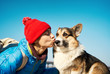 © vitaliymateha - Joyful girl taking free time with her dog outdoors, dog walking. portrait young woman in red hat kissing cute Corgi dog at sunny spring day.