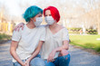 Blue hair young woman communicate with red hair teenage girl outdoor. Both wear medical mask
