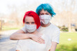 Blue hair young woman communicate with red hair teenage girl outdoor. Both wear medical mask