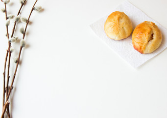 Patties on a white napkin and willow branches on white background. Bakery background. Homemade bakery. Traditional Russian pies (pirozhki), closeup. Russian cuisine. Baking for Easter. 