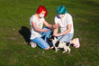 Blue hair young woman and red hair teenage girl play with puppy dog outdoor. Both wear medical mask