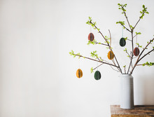Easter Holiday Home Decoration. Tree Branches In Vase With Fresh Spring Leaves Decorated With Festive Colorful Easter Eggs, White Wall Background, Copy Space. Easter Holiday Preparation, Greeting Card