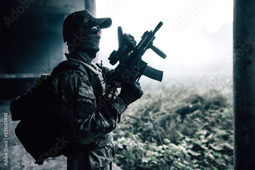 Camouflage soldier standing in a concrete building with a rifle in his hands in the jungle