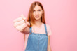 An attractive friendly girl holding out her little finger for reconciliation, promise or friendship, on a pink background