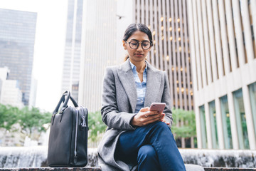 Wall Mural - Modern businesswoman browsing mobile sitting on street