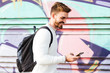 © Westend61 - Smiling man at a graffiti wall using cell phone