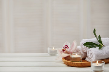 spa composition with aromatic candles, orchid flower and towel on white wooden table. beauty spa tre