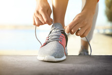 Sporty Woman Tying Shoelaces Outdoors On Sunny Day, Closeup