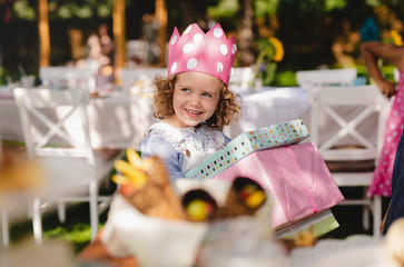 Small girl outdoors in garden in summer, holding presents.