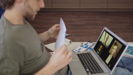 Wall Mural - tilt up side view shot of young male designer having video call with two colleagues on laptop comput