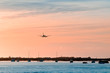 © SValeriia - The plane flies to the airport over the river in the city of Faro in Portugal. silhouettes of airplanes and airport, boats in the river, evening city...