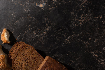 top view of cut brown bread on stone black surface