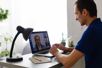 Wall Mural - Happy young man in t-shirt sitting at home, working on laptop computer, smiling.