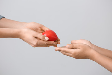 Woman giving small red heart ho little child on grey background. Concept of donations