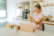 © Nebojsa - Young woman is having video call with her friends while sitting in kitchen at home. Blonde girl is using wireless headphones and smartphone to have video call with friends.