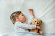 © kaloriya - Toddler baby sleeping on white sheets hugging soft brown teddy bear. Children's nap time or bedtime. Child sleep deprivation. Child sleep routine and schedule.  Top view.