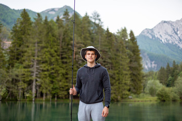 Man fishing on the pier in a beautiful lake and forest with mountains.