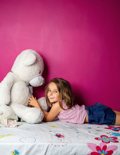 Portrait Of Little Girl With Big Teddy Bear In Front Of Pink Wall