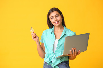 Poster - Young woman with laptop and credit card on color background. Online shopping concept