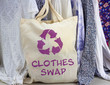 Leinwandbild Motiv Clothes swap reusable bag with recycle textiles symbol in front of rack of clothes. Recycle clothes for sustainable living.