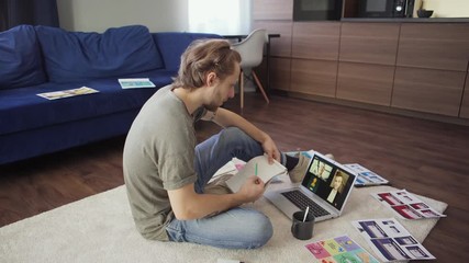 Wall Mural - Side view shot of young marketing specialist having video call with two colleagues on laptop computer and drinking coffee sitting on floor at home surrounded by papers