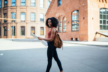 Black cheerful female holding map exploring city