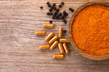 tumeric powder l with curcuma capsules and black pepper ( peppercorns or piper nigrum )  isolated on wood table background. Top view.