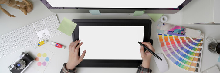Overhead shot of female graphic designer drawing on mock-up graphic tablet, computer and designer supplies