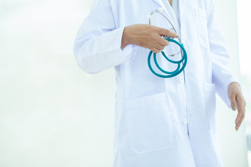 Wall Mural - Asian Young   woman  doctor or nurse in white uniform scrubs holding Stethoscope standing in front of a white wall in the hospital,