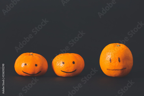 One citrus fruit with drawn neutral face among happy ones on dark background. Concept of depression