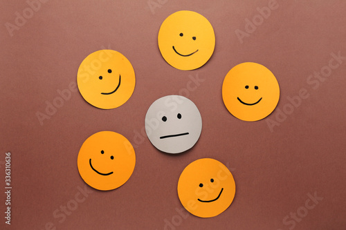 One neutral face among happy ones on color background. Concept of depression